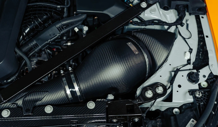 A high-performance carbon fiber cold air intake installed in a clean, modern car engine bay.