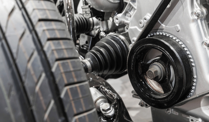 A close-up view of a car's engine pulley, serpentine belt, CV axle, and high-performance tire.