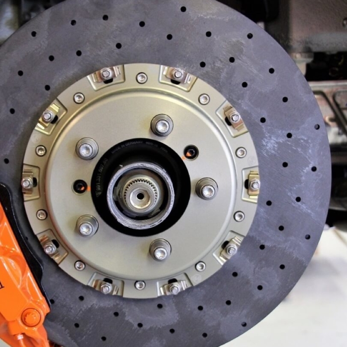 A close-up of a drilled, two-piece high-performance brake rotor and a large orange brake caliper.